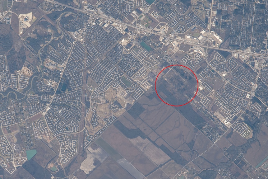 A satellite image of a town in Texas shot from space, with a red circle highlighting an empty green space 