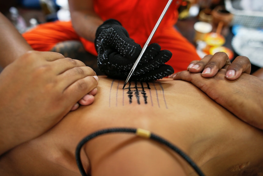 Close up of a a traditional needle being used to tattoo the body of a man.