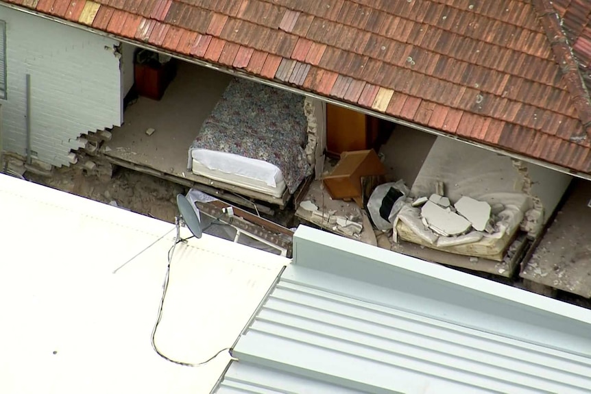 Beds can be seen inside a home where the wall has collapsed