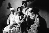 Four members of band Mdou Moctar wear African robes, sit together and look at the camera