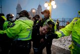 Man arrested, lifted into the air by several police officers and carried away, while snow falls