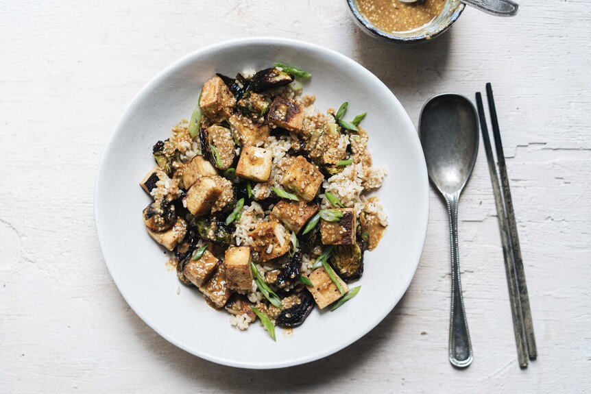 A bowl of brown rice, crispy tofu and brussels sprout salad topped with sesame dressing, a healthy vegetarian salad recipe.