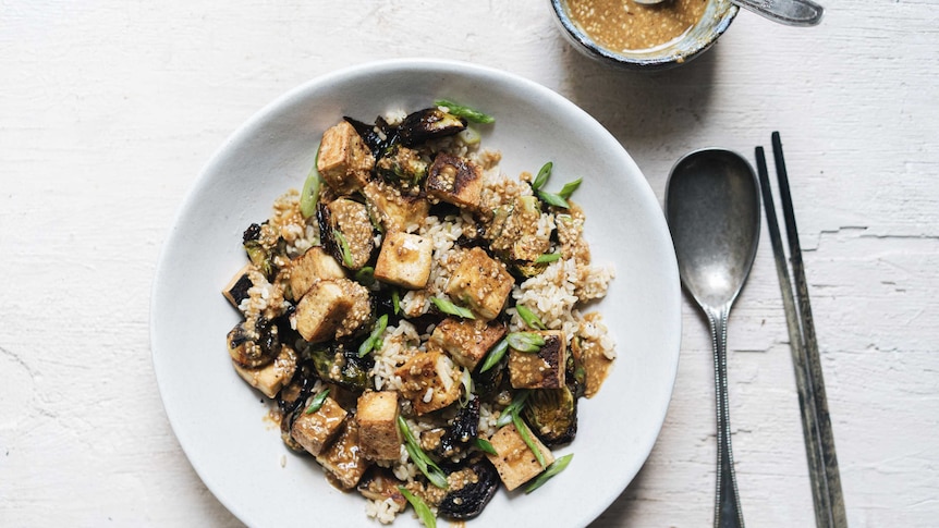 A bowl of brown rice, crispy tofu and brussels sprout salad topped with sesame dressing, a healthy vegetarian salad recipe.