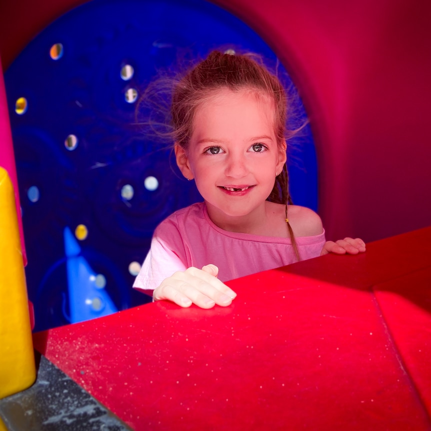 A young girl smiles from inside colourful play equipment.