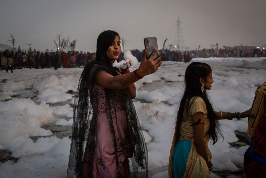 A Hindu devotee takes a selfie while holding handful of chemical foam she picked