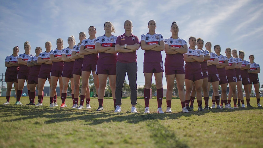 Members of the Queensland women's State of Origin team stand with arms folded, in 'V' formation