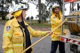 Woman and young man in firefighting uniform winding hose on truck