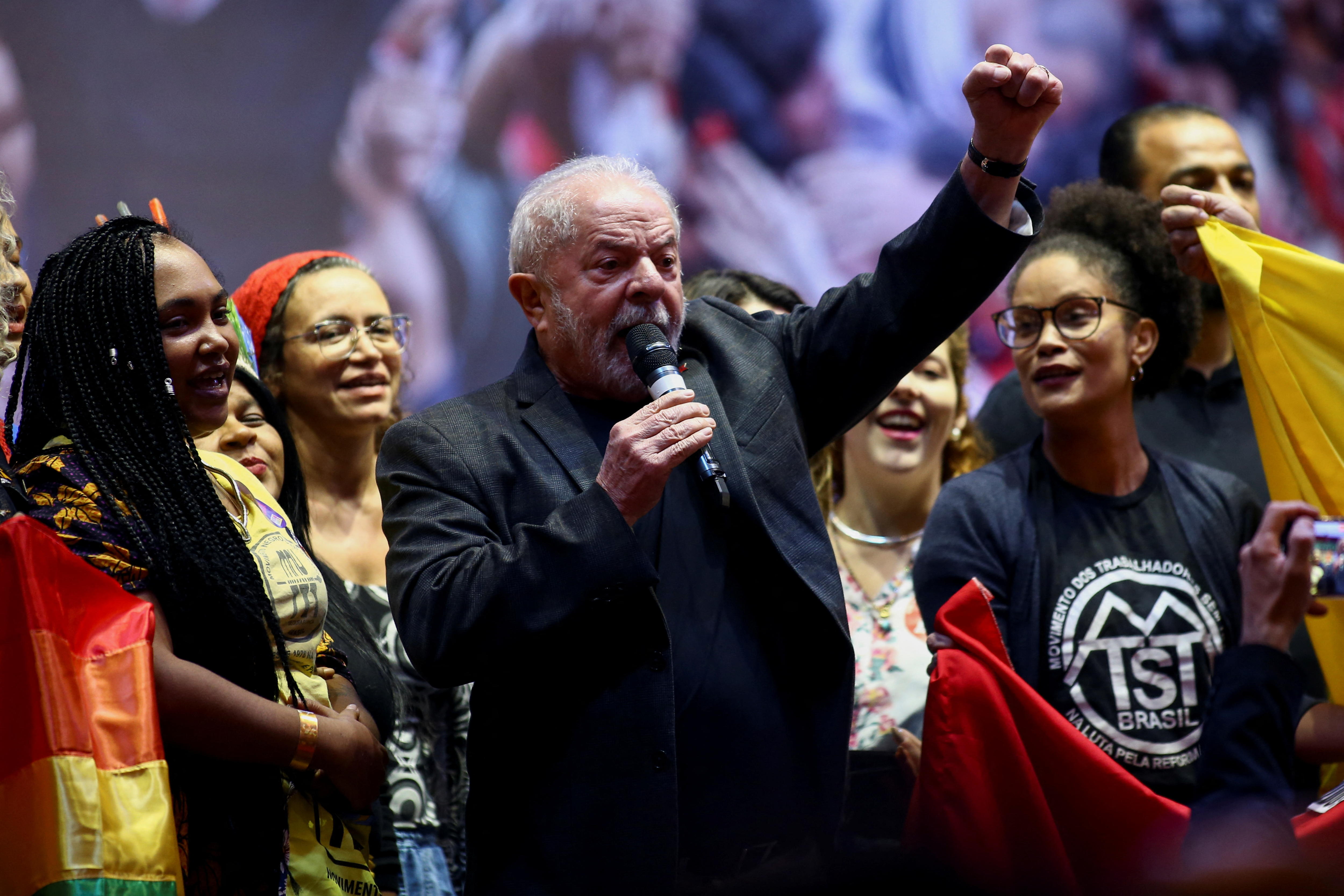 Brazil's former President Luiz Inacio Lula da Silva speaks into a mic as a group of women look on