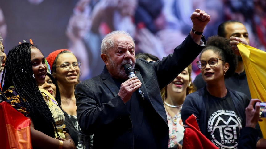 Brazil's former President Luiz Inacio Lula da Silva speaks into a mic as a group of women look on