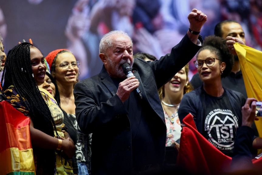 Brazil's former President Luiz Inacio Lula da Silva speaks into a mic as a group of women look on