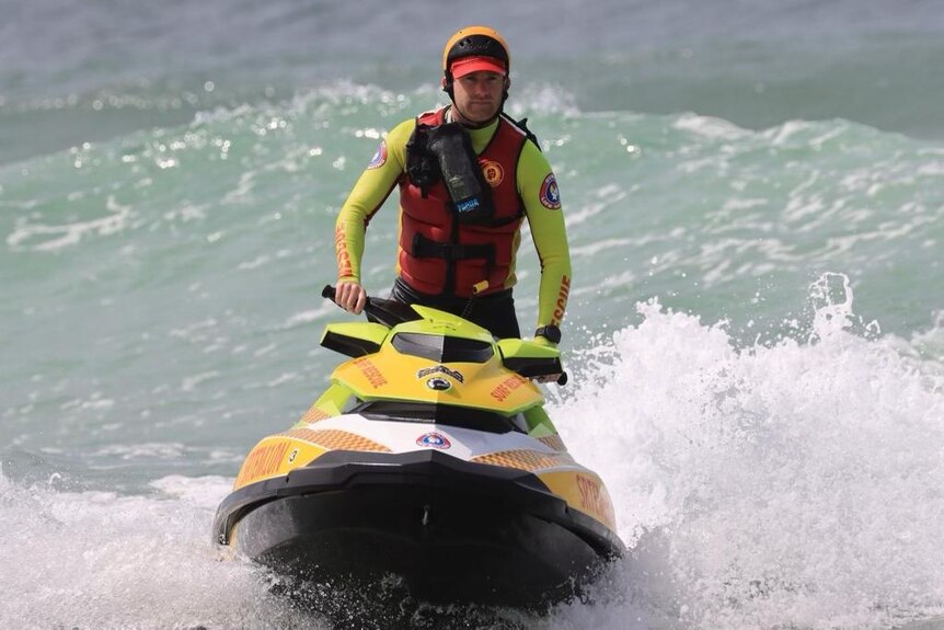 a man in life saving uniform on a jetski in the surf.