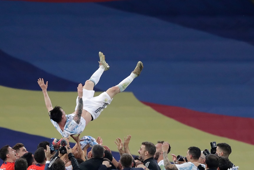 Argentina's soccer team stands around laughing as they throw Lionel Messi in the air in celebration of their Copa America title.