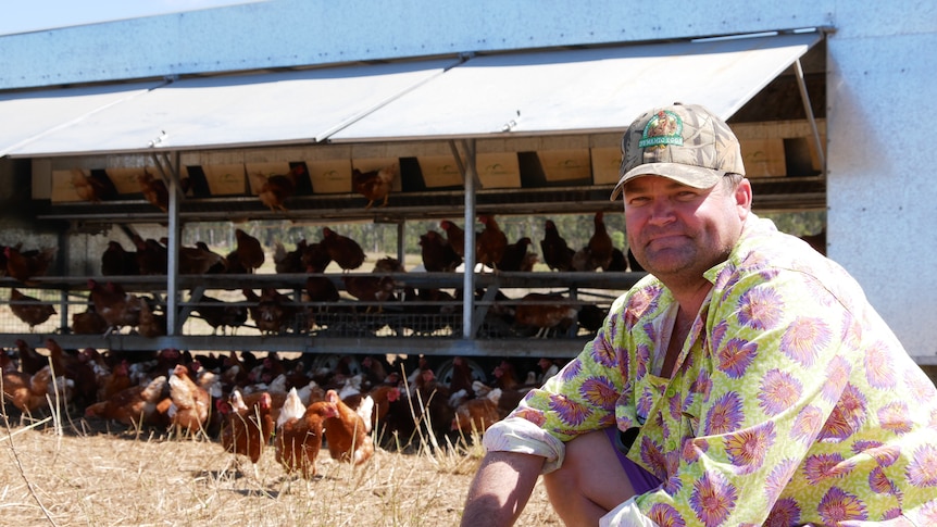 A man smiles at the camera. Chickens in a shed are in the background.