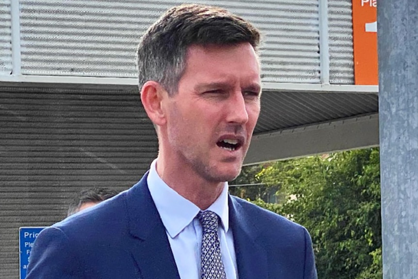 Queensland Transport Minister Mark Bailey speaking to the media on a train station platform.