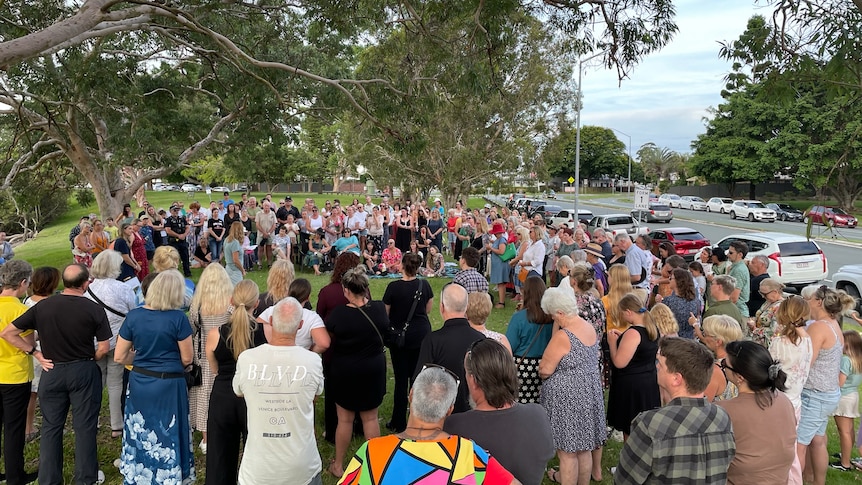 A large group of people is pictured standing in a circle for a candlelit vigil.