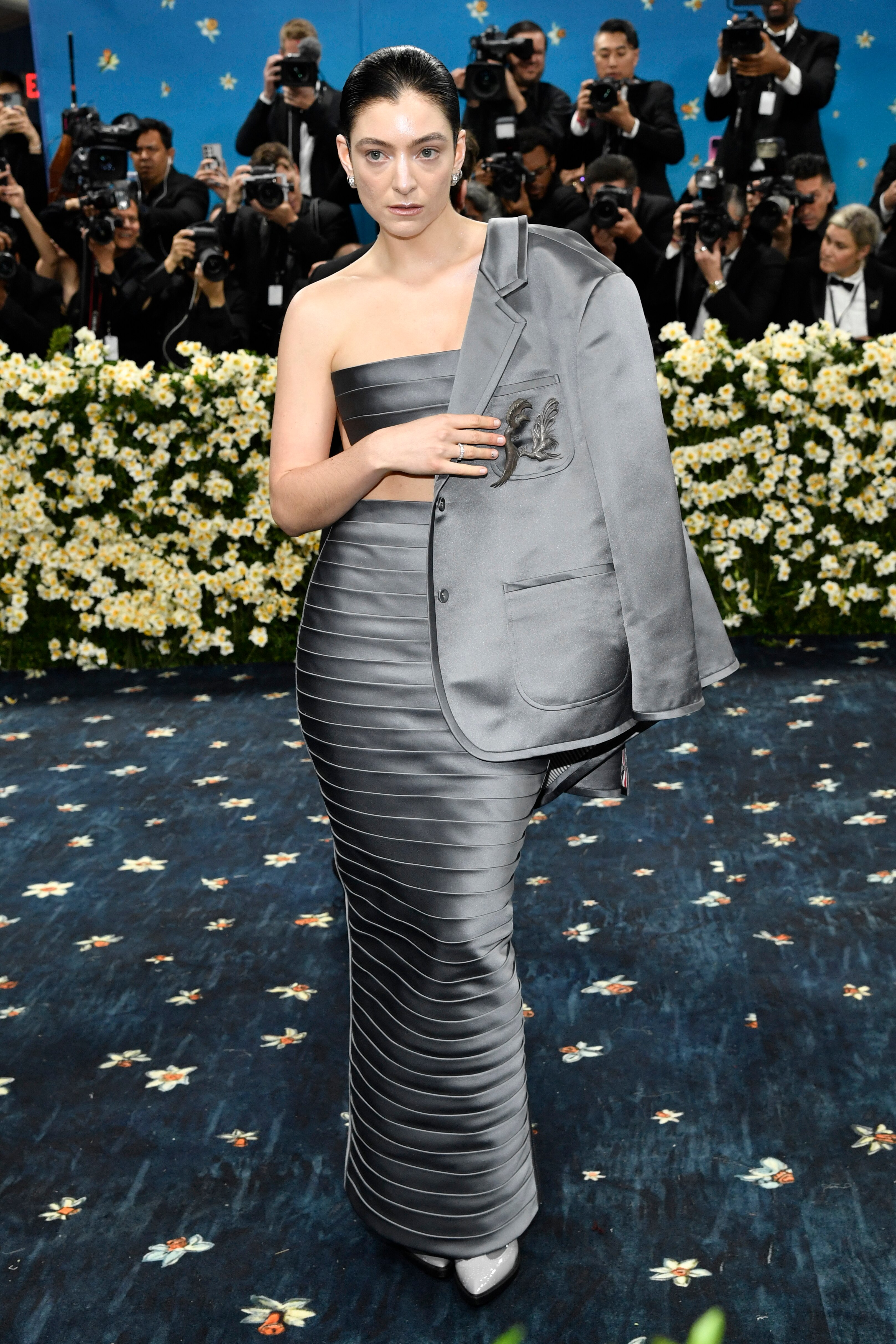 Lorde wearing a silky grey skirt with matching chest piece and a matching suit jacket over one shoulder