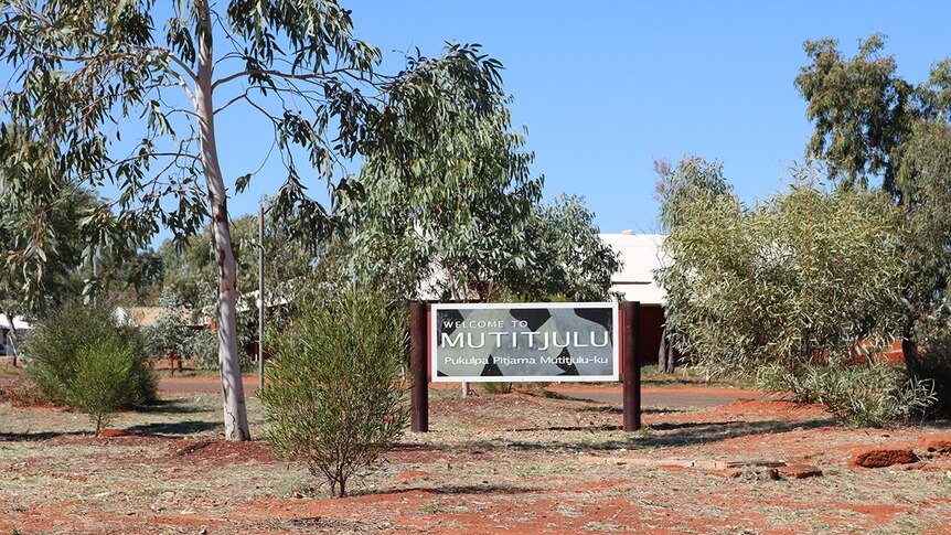 A "Welcome to Mutitjulu" sign surrounded by trees at the entrance to the town.