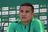 Tim Cahill sits in front of a sponsor board with his arms folded.