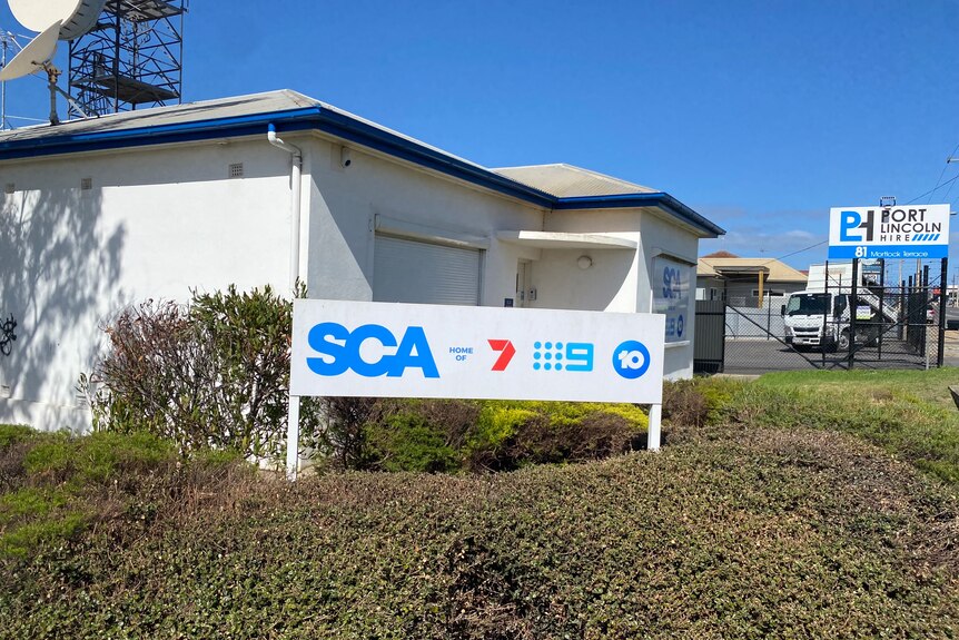 A modest, residential-looking building with a sign that says "SCA" and features the logos of several television networks.