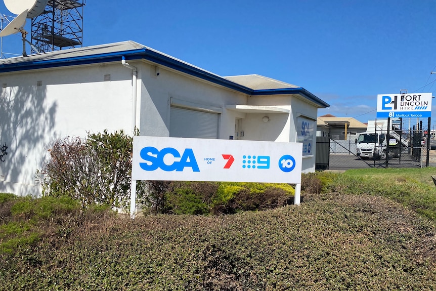A modest, residential-looking building with a sign that says "SCA" and features the logos of several television networks.