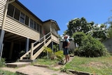 A man stands with his hands on his hips looking towards his tall house