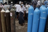 Industrial oxygen containers stand in front of a crowd of people on an Asian street.