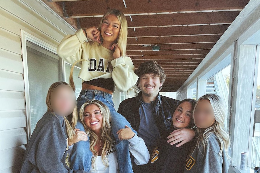 Five young women and a man stand together for a photo on a porch