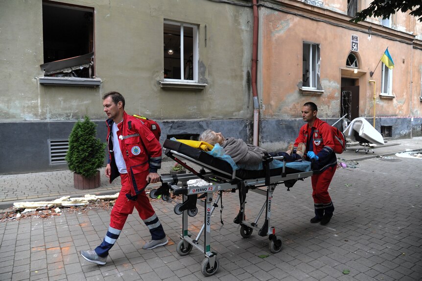 two emergency workers wearing red carrying a woman on a stretcher through a street