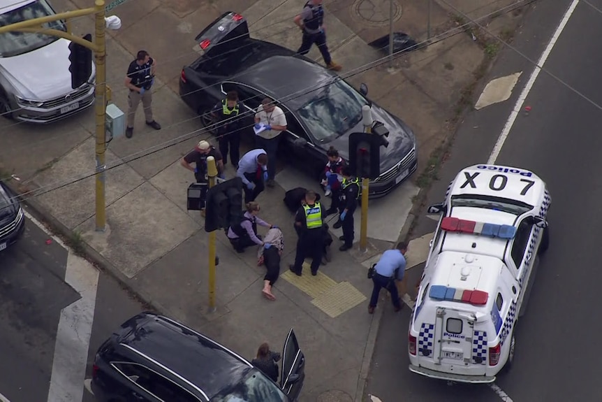 An aerial view shows a man being arrested by police on a traffic island of a busy street.