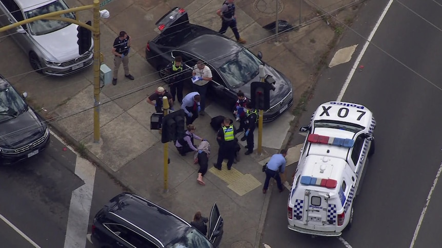 An aerial view shows a man being arrested by police on a traffic island of a busy street.