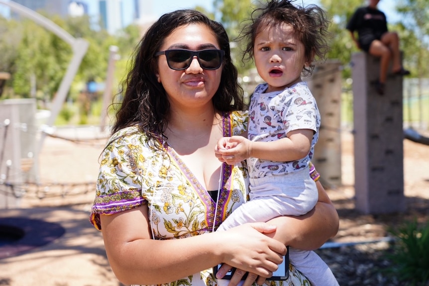 A mum and her infant child pose for a family photo in an outdoors setting