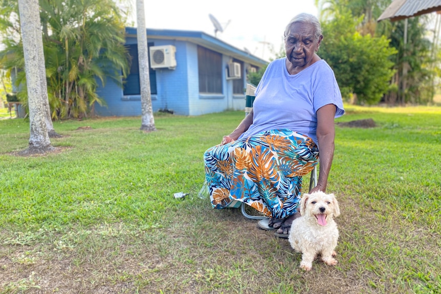 an aboriginal woman patting a white dog on a lawn