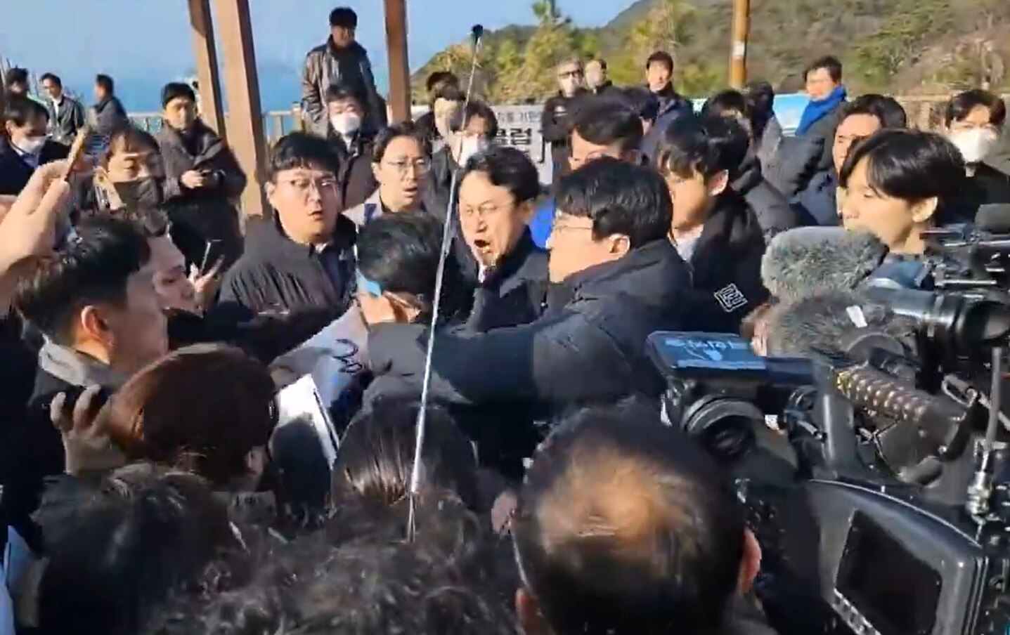 A Korean man in suitgrabs another man in the middle of a tightly packed crowd.