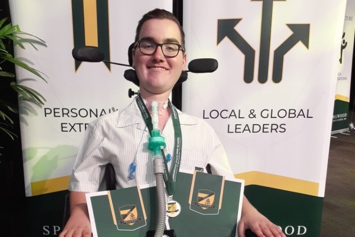 A young man in a wheelchair smiling after receiving a number of awards at an awards event.