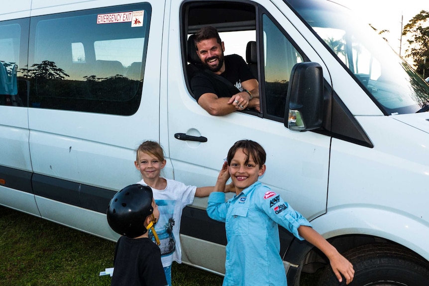 Jonny Dustow in the driver's seat of the van that is his home with some unknown children standing alongside the van