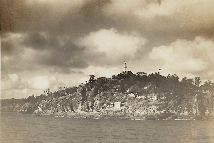 Black and white photo of a lighthouse on a island cliff.