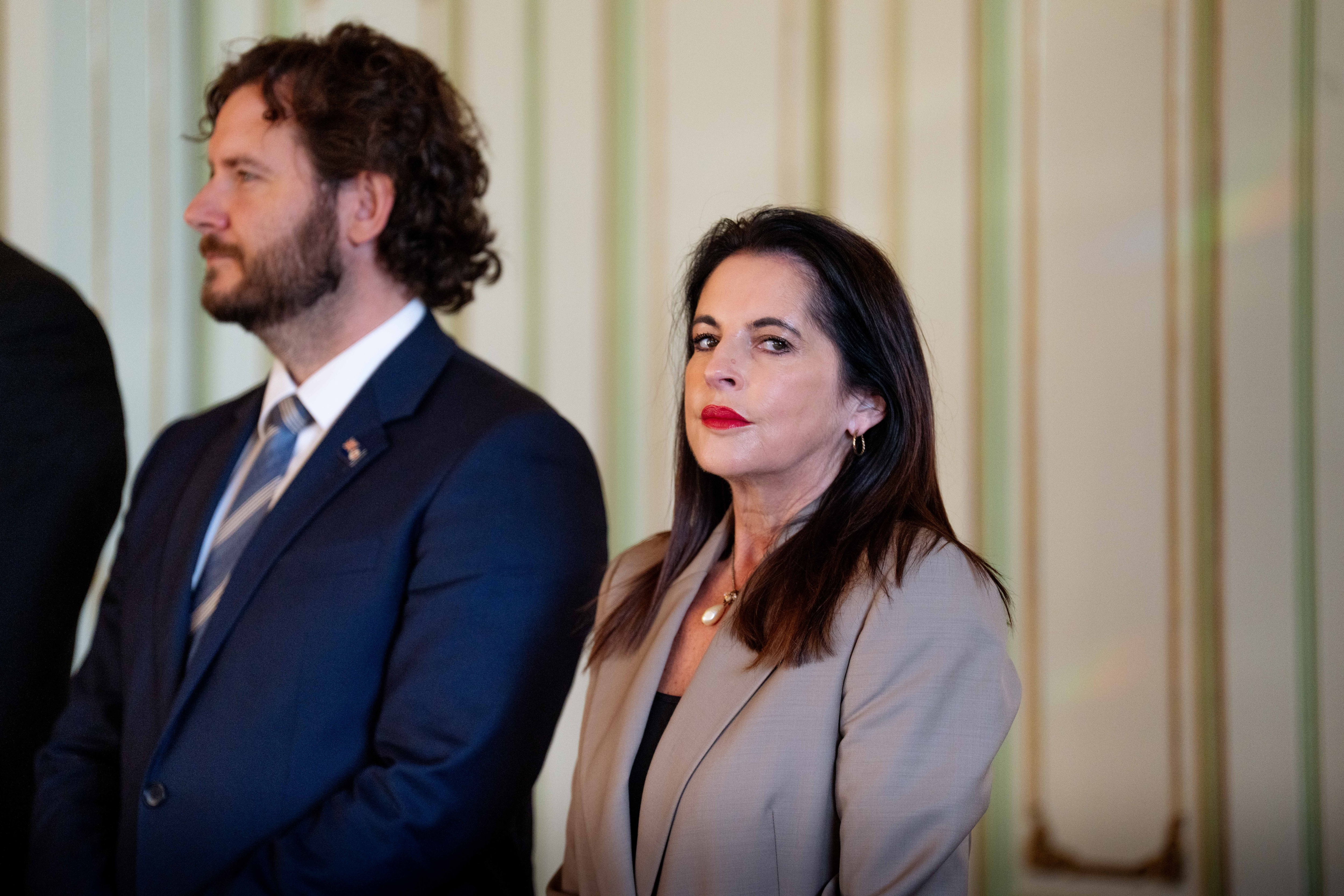 A woman dressed formally looks to the distance, next to men in suits
