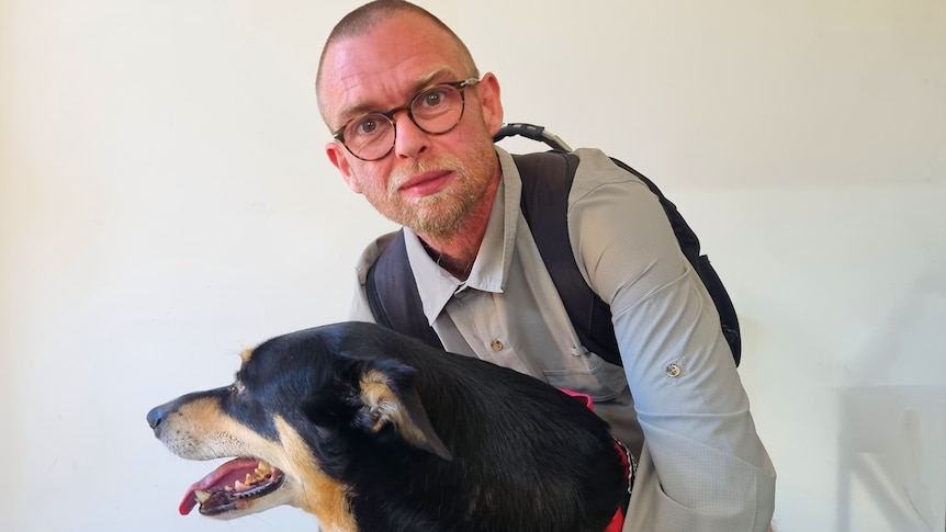 A man in glasses hugs a dog.