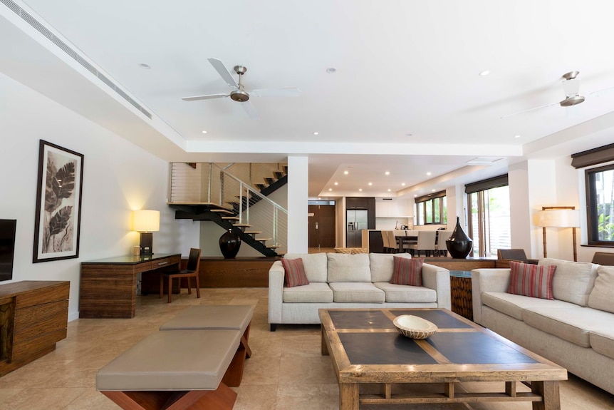 A roomy lounge room with fans and beige and brown cushioned couches.