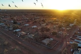 An aerial view of a remote town with houses on wide, red-dirt blocks.
