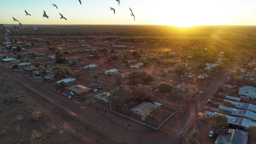 An aerial view of a remote town with houses on wide, red-dirt blocks.