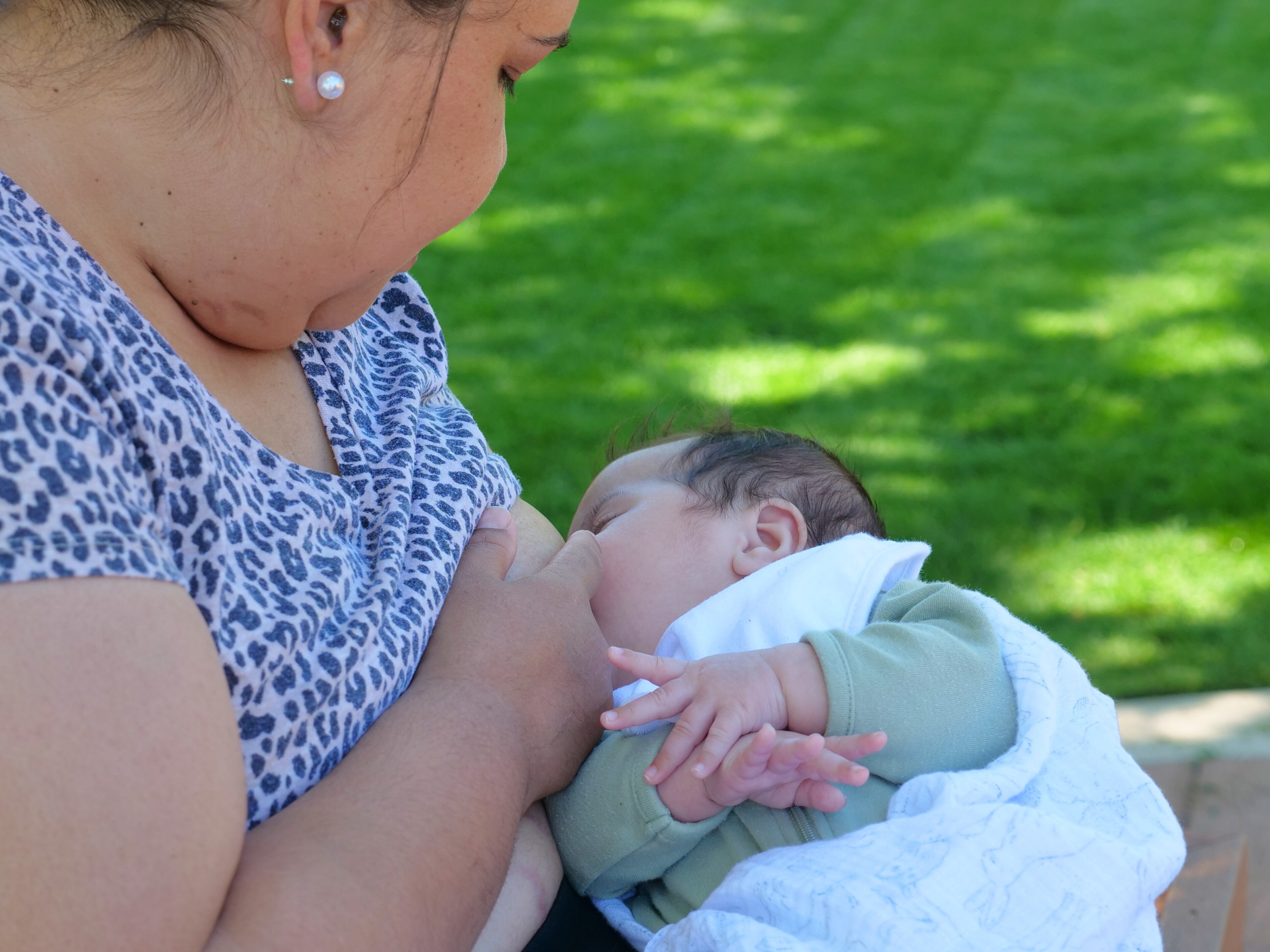 a woman breastfeeding her baby, side angle, grass in the background