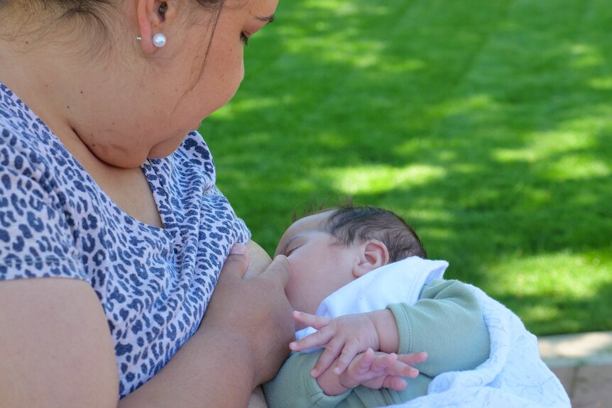a woman breastfeeding her baby, side angle, grass in the background