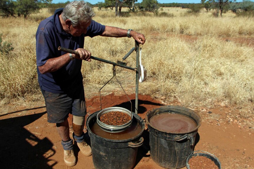 A grey haired man dipping rocks in water to wash them