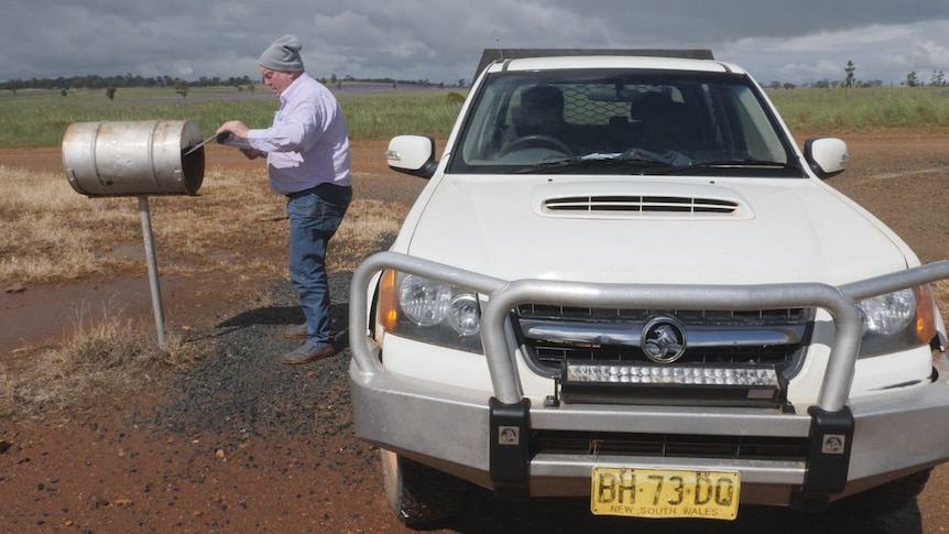 A man puts a letter in a metal box next to his ute.
