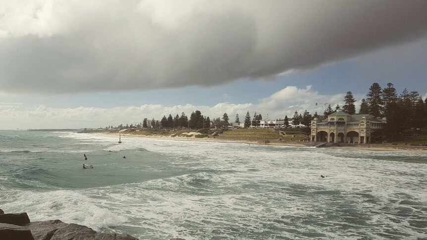 Dark clouds loom over the foreshore at Cottesloe Beach in Perth with a few surfers in the water.