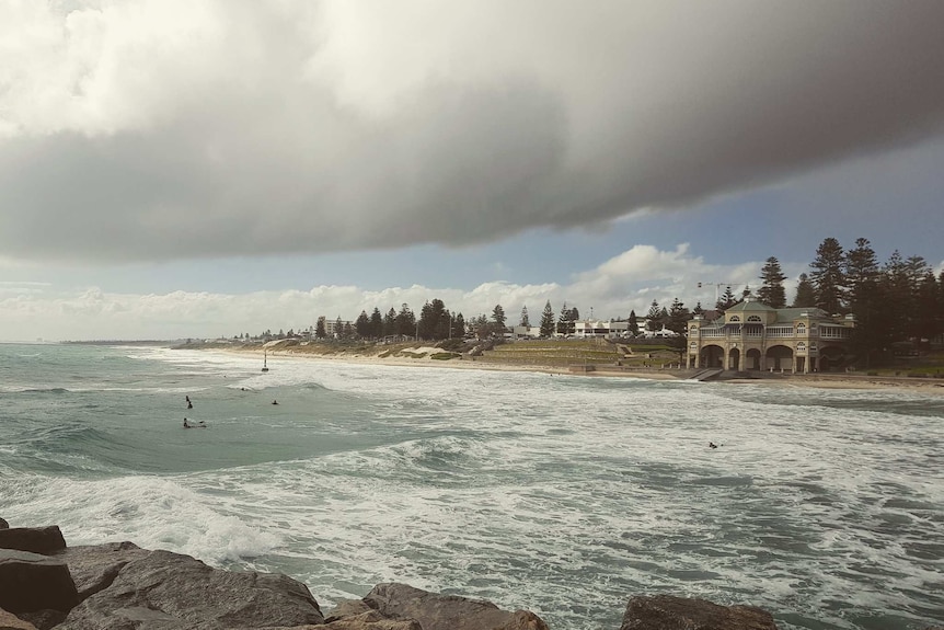 Dark clouds loom over the foreshore at Cottesloe Beach in Perth with a few surfers in the water.