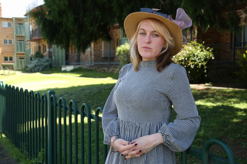 Charlotte leaning against a fence looking sternly at the camera.