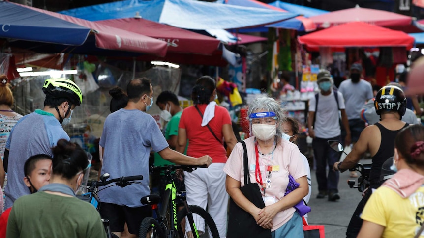 A woman wearing a face shield and a face mask walking down a crowded street.