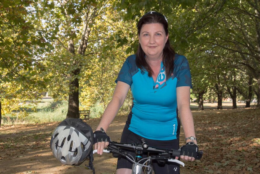 A woman in cycling gear standing still on a bike in a park